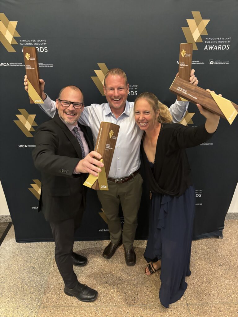 Three smiling people hold up trophies in celebration, posing in front of a backdrop that reads Vancouver Island Construction Association Awards. Proud winners from Falcon Heights celebrate their achievements as Custom Home Builder at the 2026 VIBI Awards.